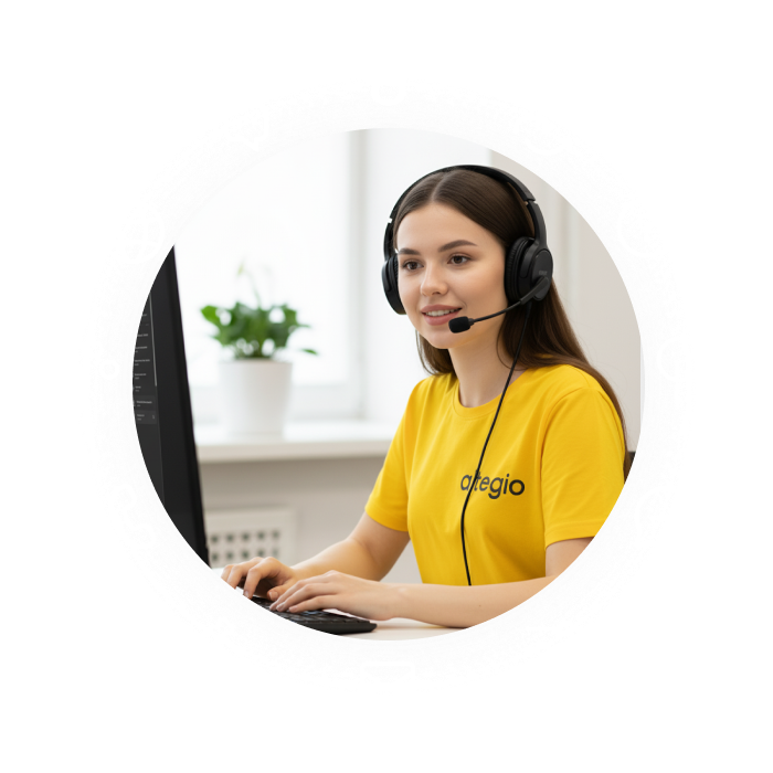 A young woman wearing a yellow shirt and headset, working at a computer in a bright office.